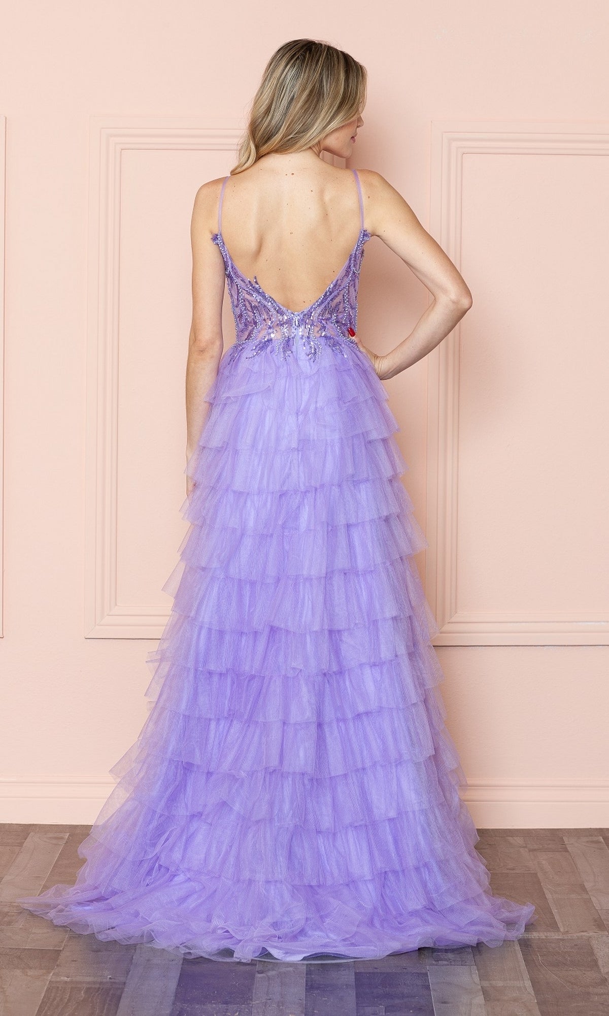 A woman faces away wearing the Open-Back Long Ruffled Prom Dress: Poly USA 9408, a lilac gown with a deep V-back, spaghetti straps, and layered tulle for an elegant formal evening look.